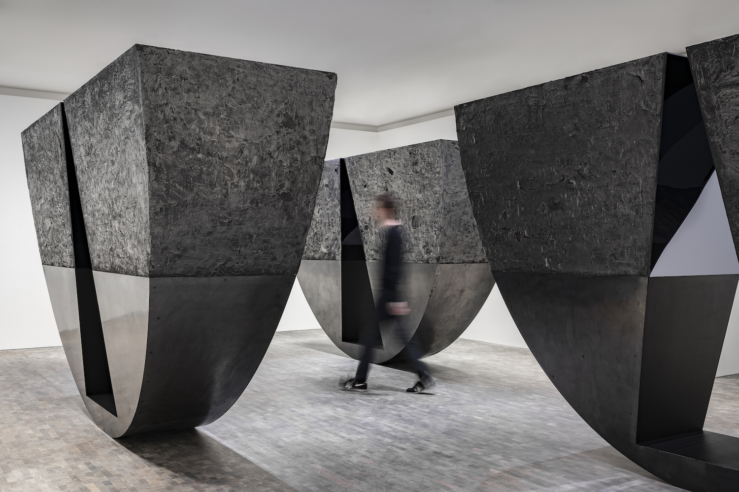 Installation view of person walking through three structures in Torkwase Dyson's “Liquid a Place” artwork