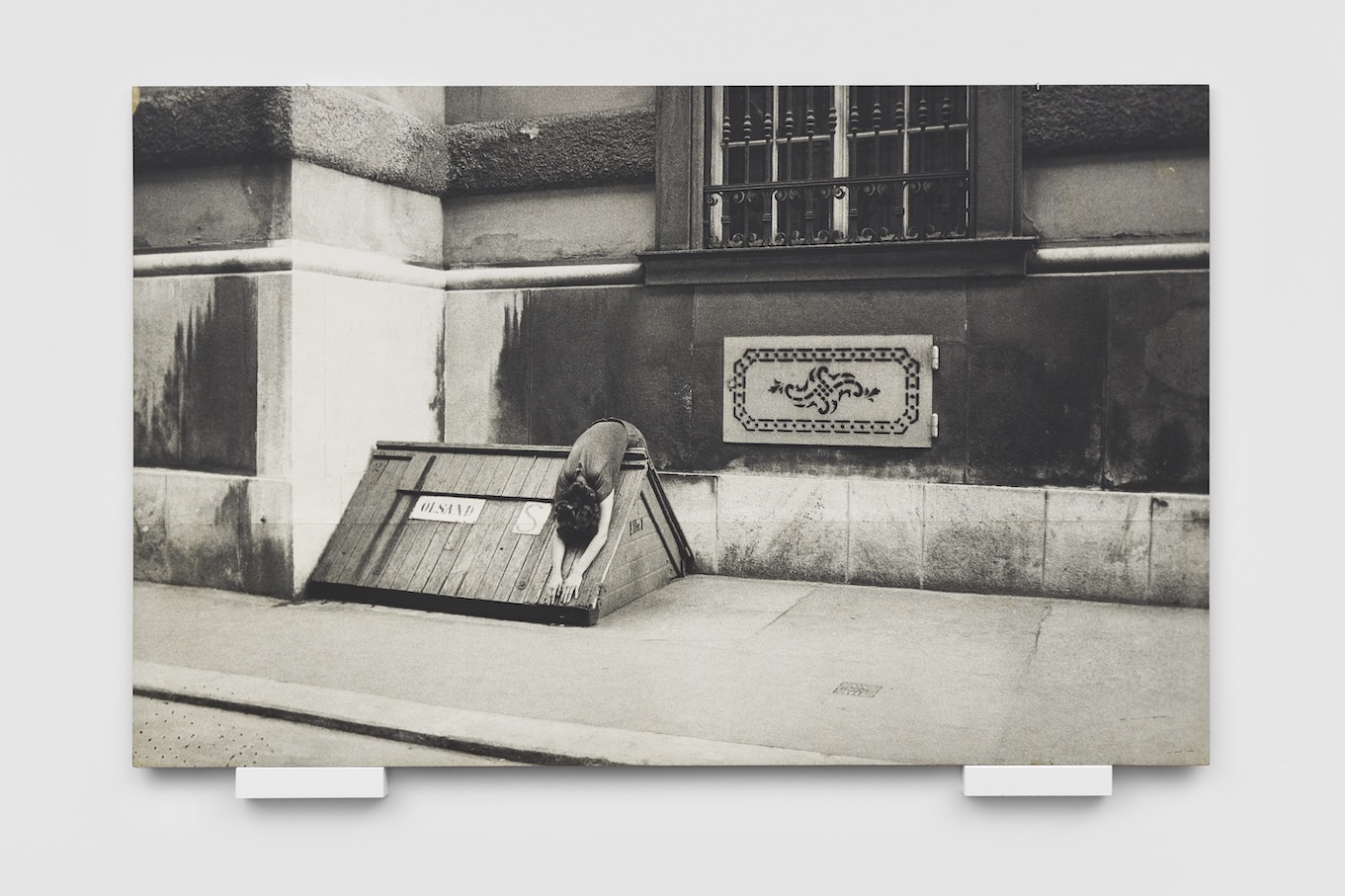 Black and white image of a woman draped over the built environment on a sidewalk in Vienna