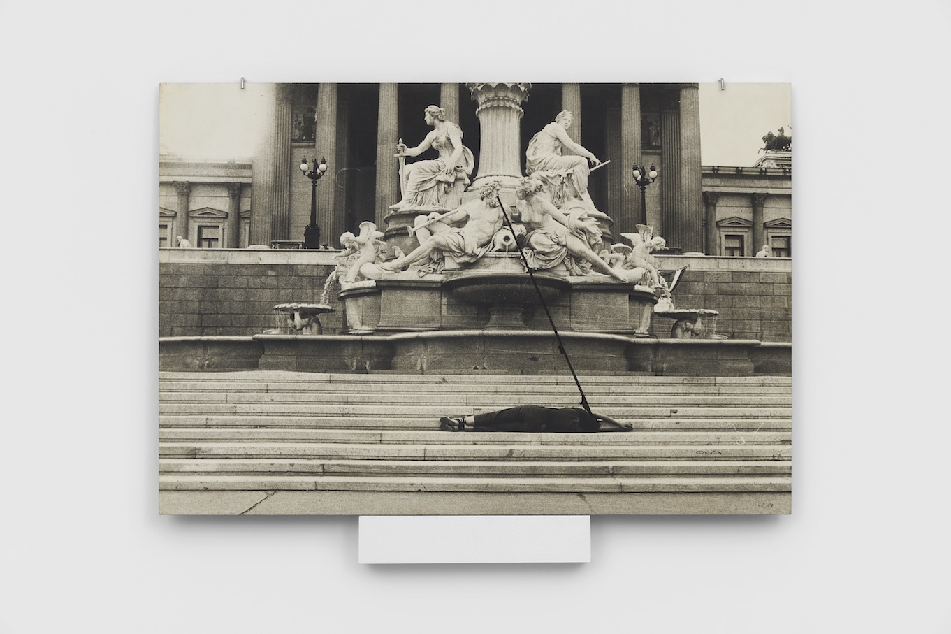 Black and white image of woman lying down on the steps leading up to an ancient statue, facing her face to that of a man in the statuetoward the statue with a black line connecting 