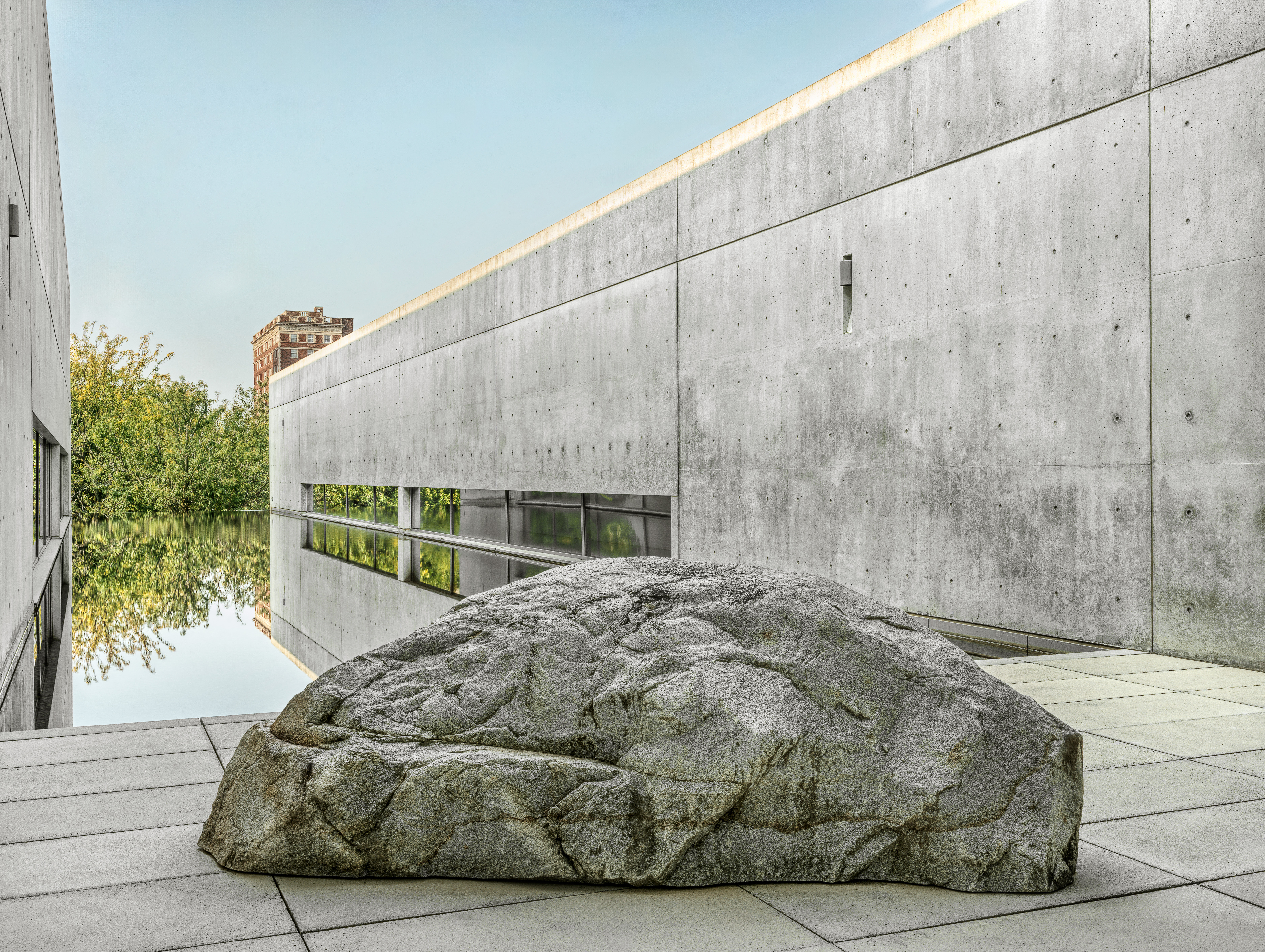 Scott Burton bench carved out of large rock on a connecting pathway between two branches of a concrete building sitting on a body of water