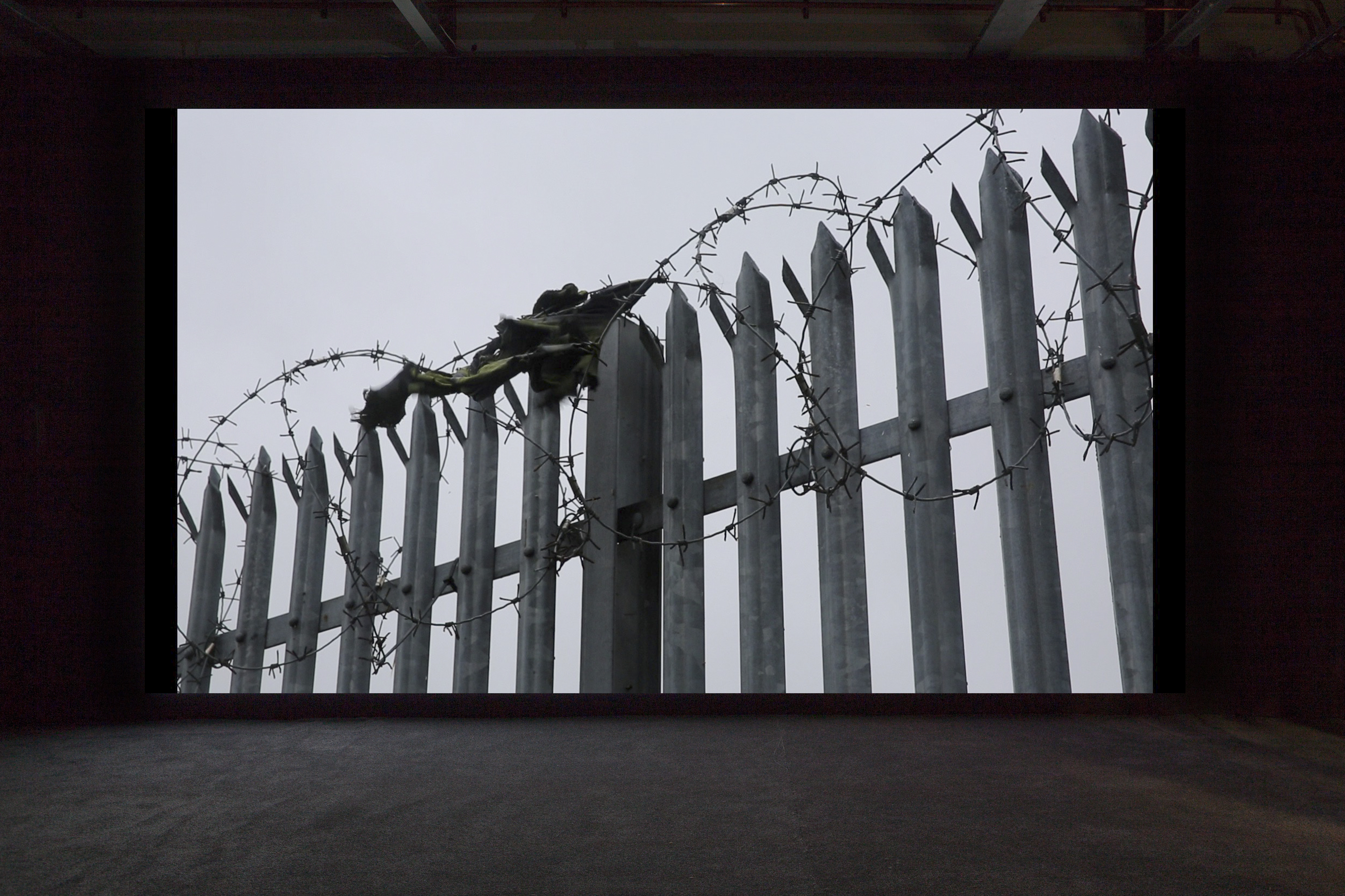 A film still of a fence topped with barbed wire.