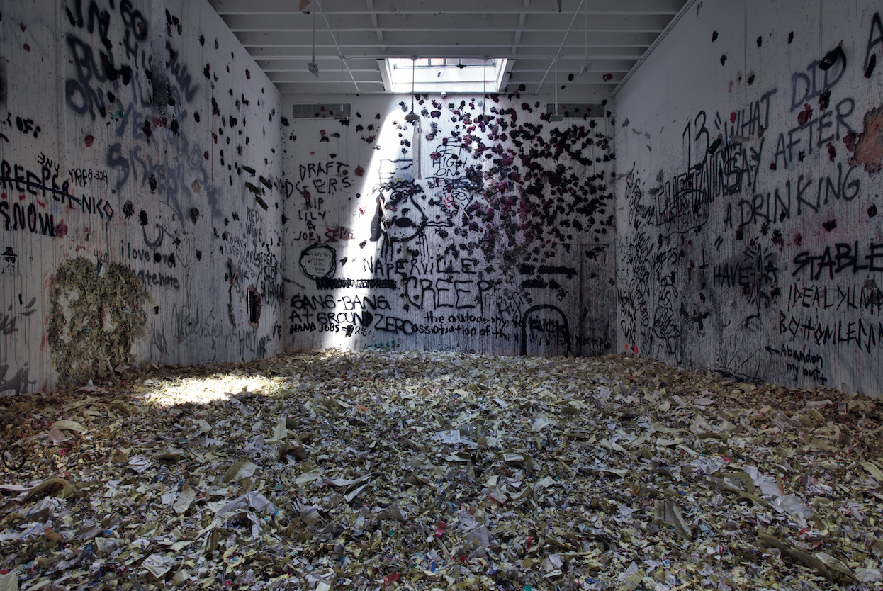 A gallery with a skylight filled with trash with graffiti on the walls