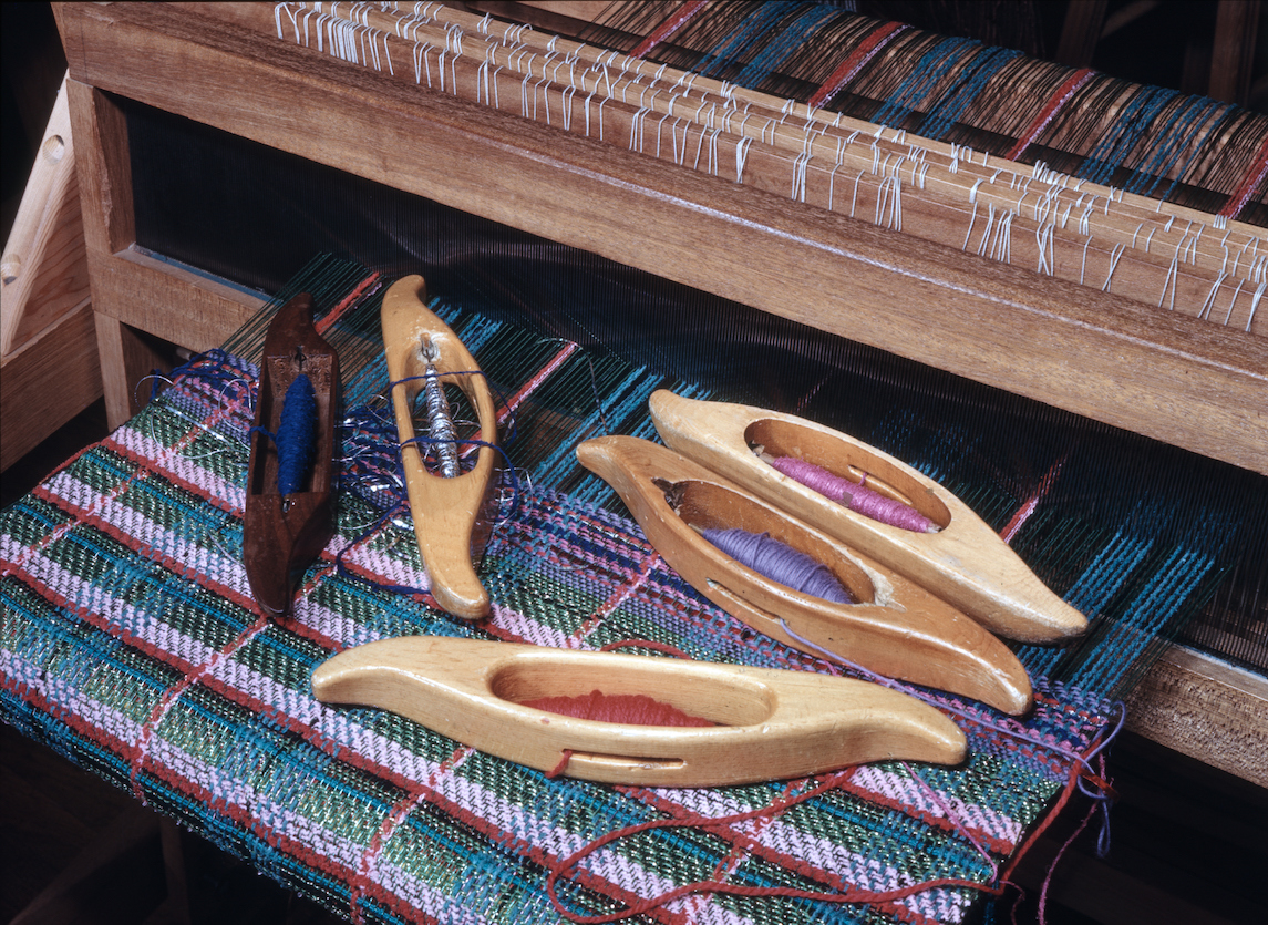 colorful threads and textile in progress on loom with five wooden shutters