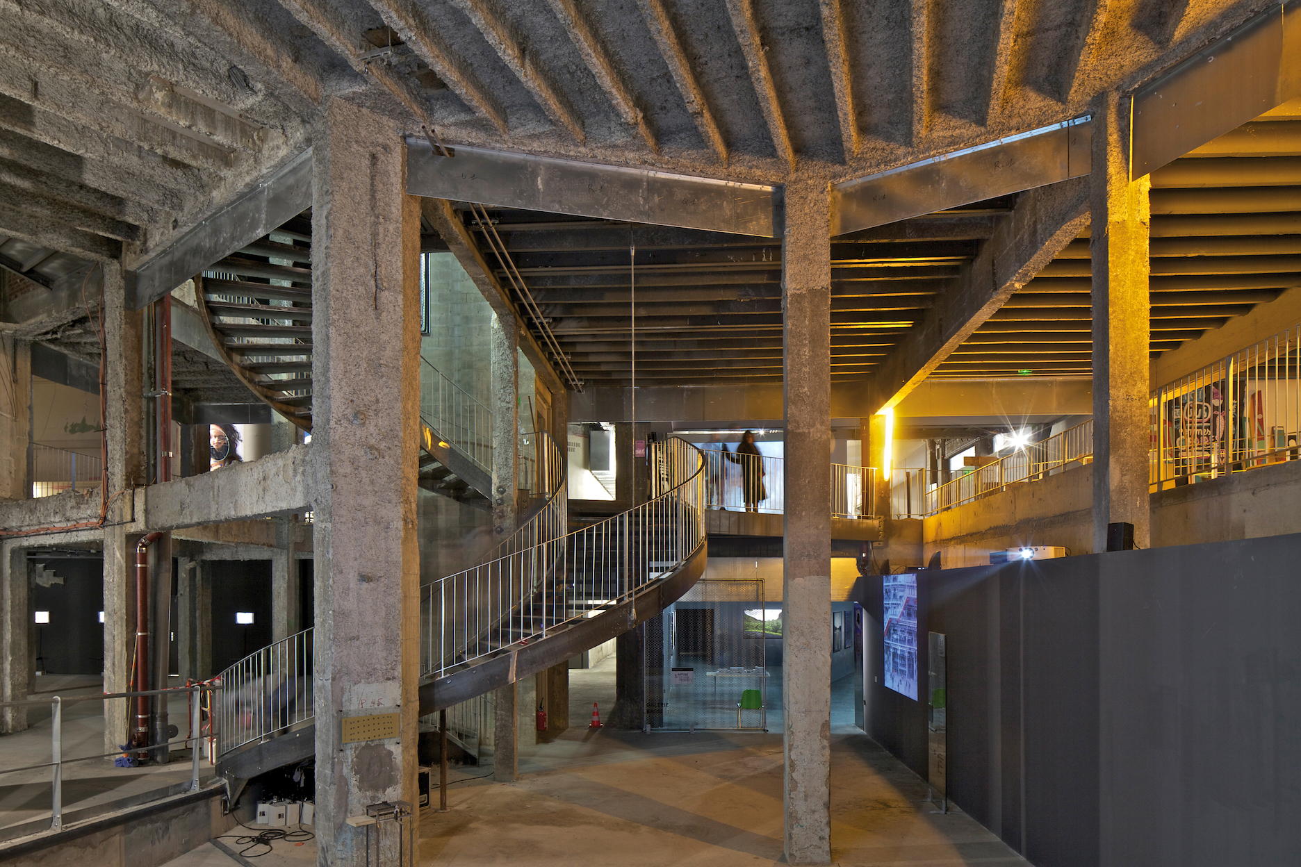 wide shot of Lacaton and Vassal's Palais de Tokyo concrete architecture with metal spiral staircase