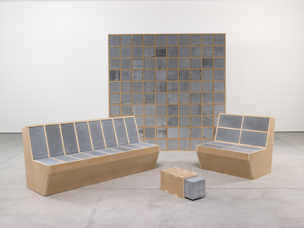 Four pieces of minimalist gray and light brown furniture on display in an exhibit