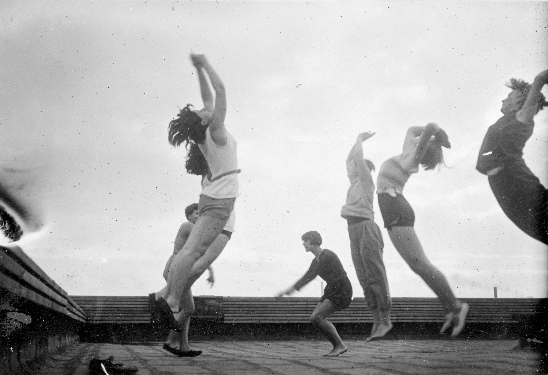 Black and white photograph of seven women facing each other and jumping in a rooftop aerobics class