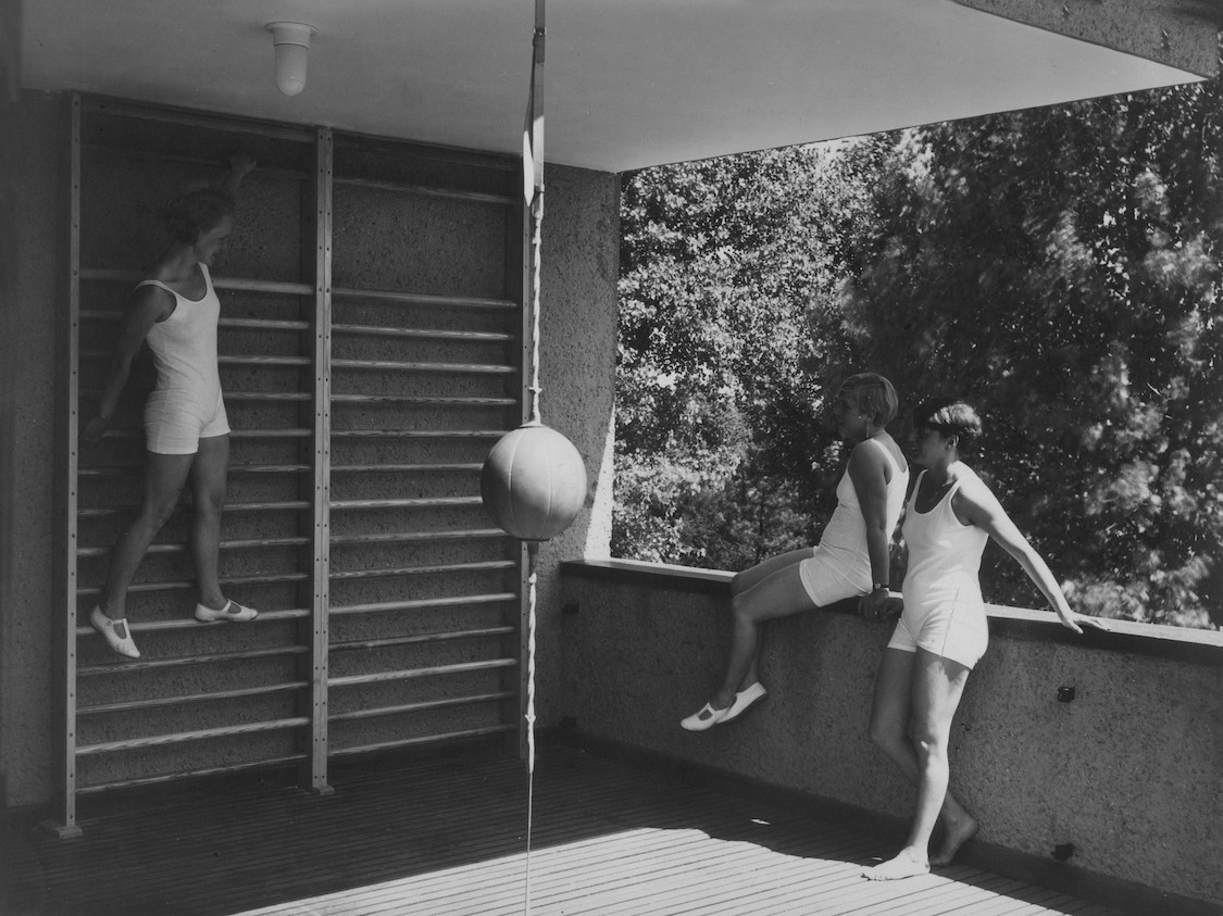 Black and white photograph of three women on a second-story terrace that has been transformed into a gym