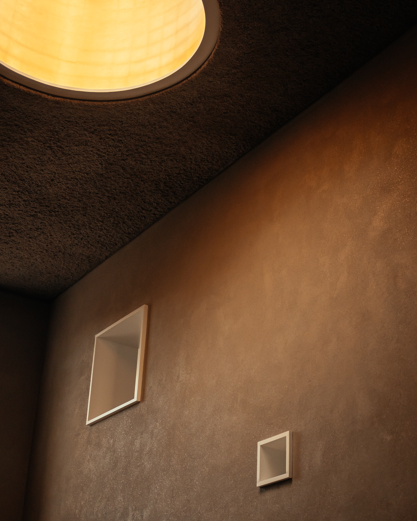 A close up of a brown wall with two small windows in it and a brown ceiling with a hole in it for a Christmas tree