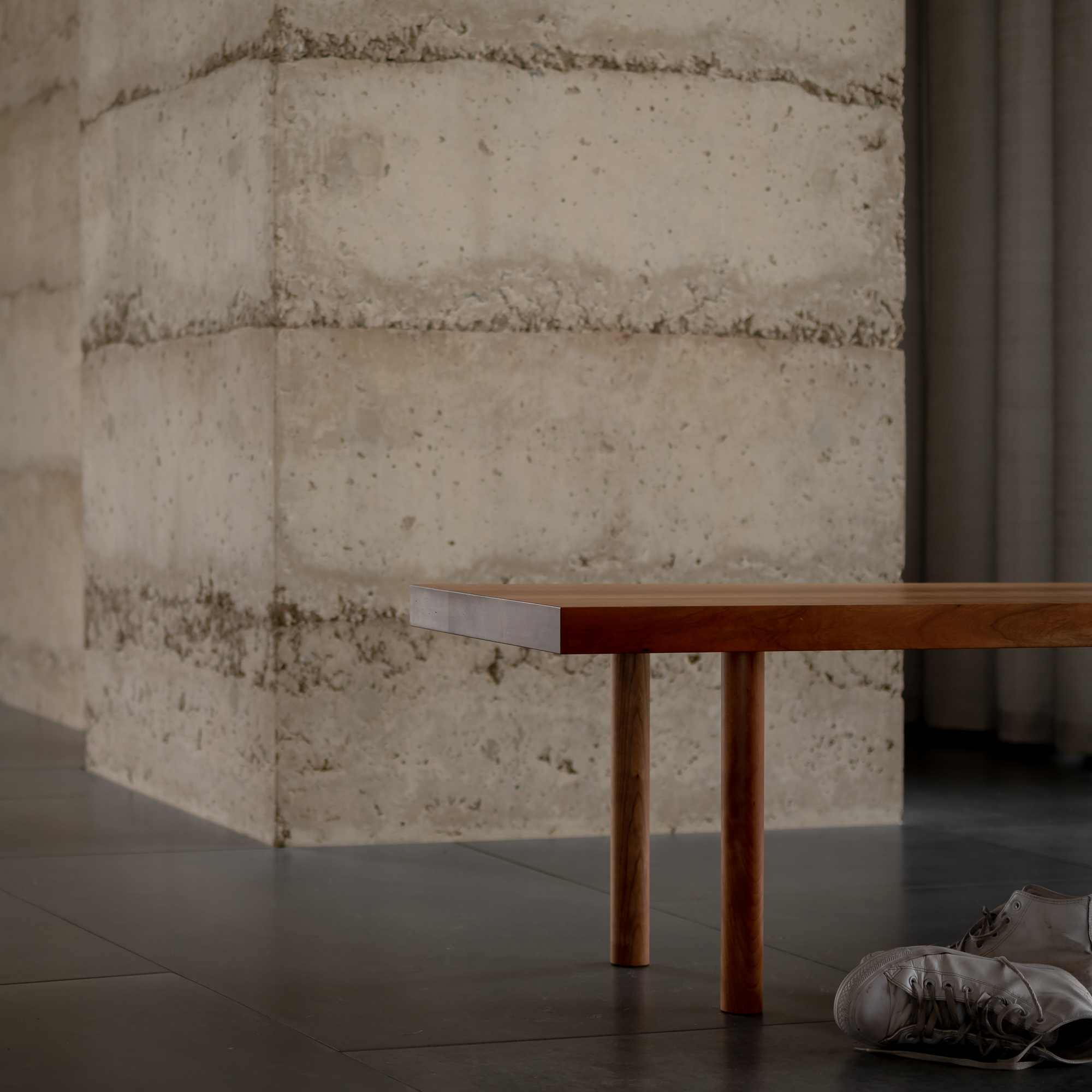 Close up of brown shoes under a brown wooden bench against a concrete wall